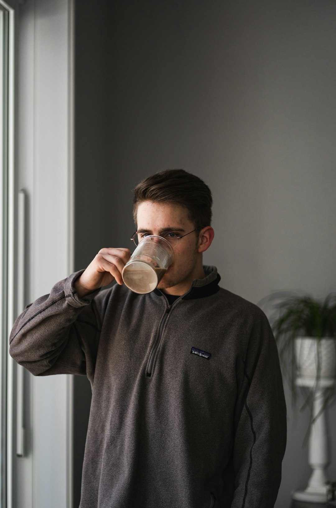 man in gray sweater drinking from clear drinking glass