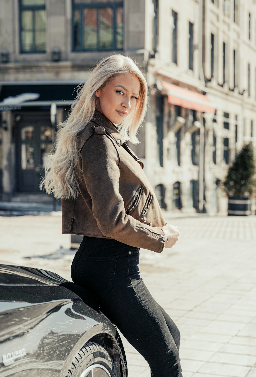 woman in brown coat and black pants sitting on sidewalk during daytime