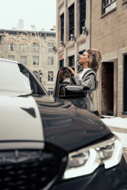A professional driver standing beside a clean, well-maintained car in a modern urban setting.