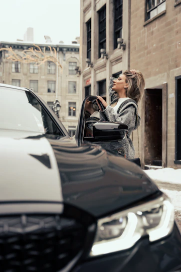 A professional driver standing beside a clean, well-maintained car in a modern urban setting.