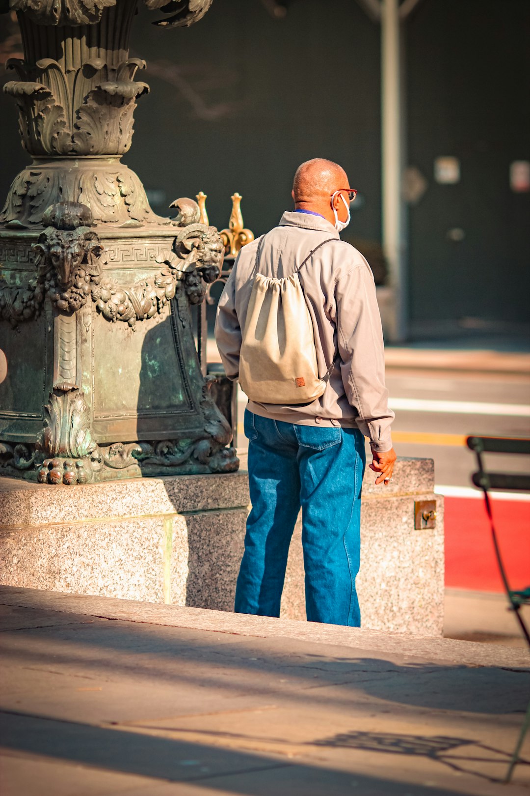 man in brown dress shirt and blue denim jeans standing near black statue during daytime