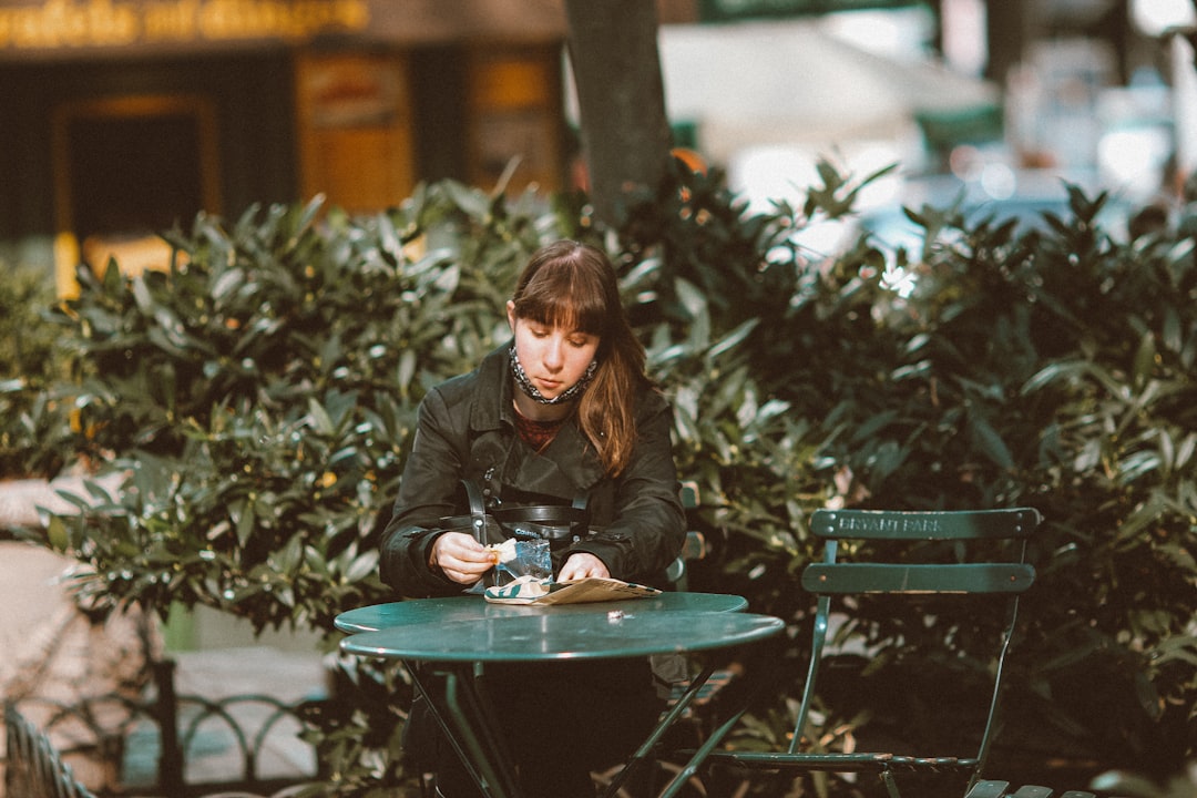 woman in black leather jacket sitting on green wooden bench during daytime
