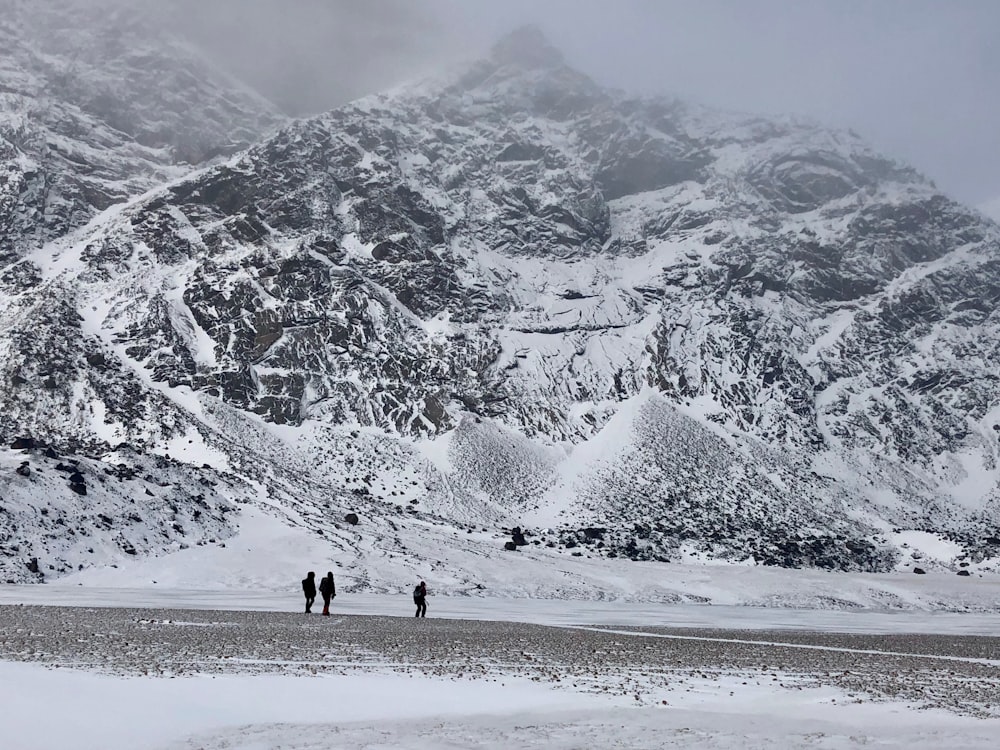 2 pessoas andando em solo coberto de neve perto da montanha coberta de neve durante o dia