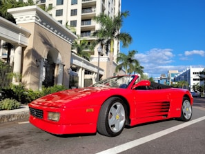 A shiny red convertible parked along the sunny California coast with palm trees in the background.