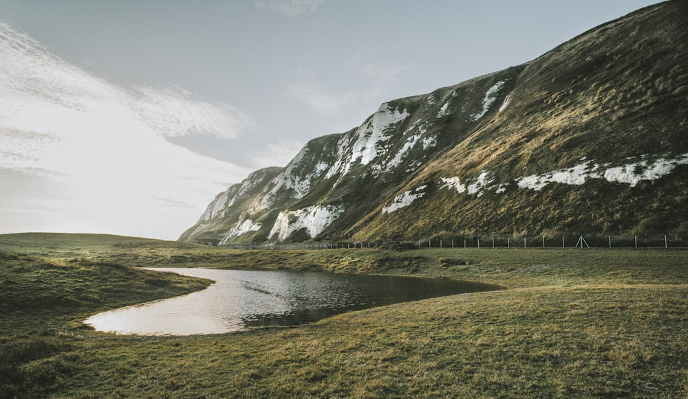 lake in the middle of green grass field and mountains