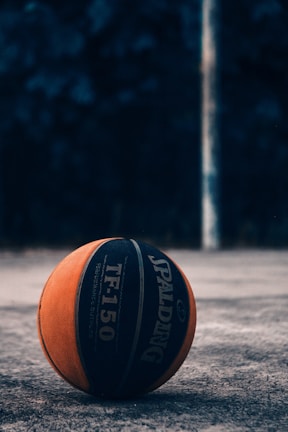 A vibrant basketball spinning on a player's fingertip on an outdoor court.