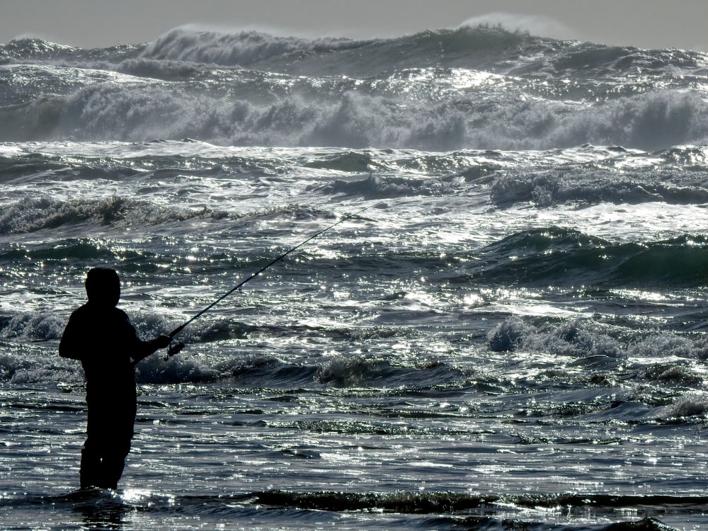 man fishing on sea waves during daytime