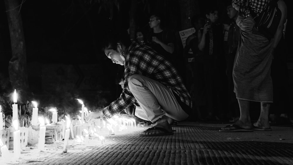 Hombre con camisa a cuadros y pantalones sentado en el suelo con velas encendidas