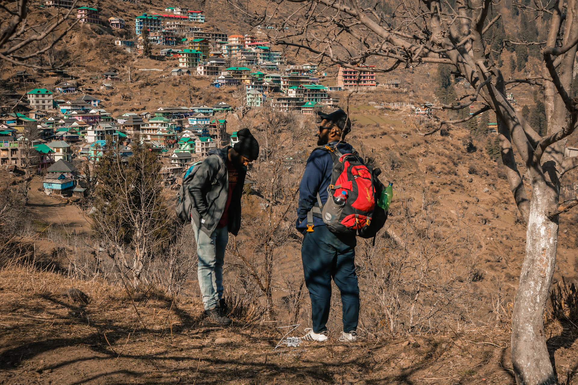 man in black jacket and gray pants with red backpack walking on brown field during daytime