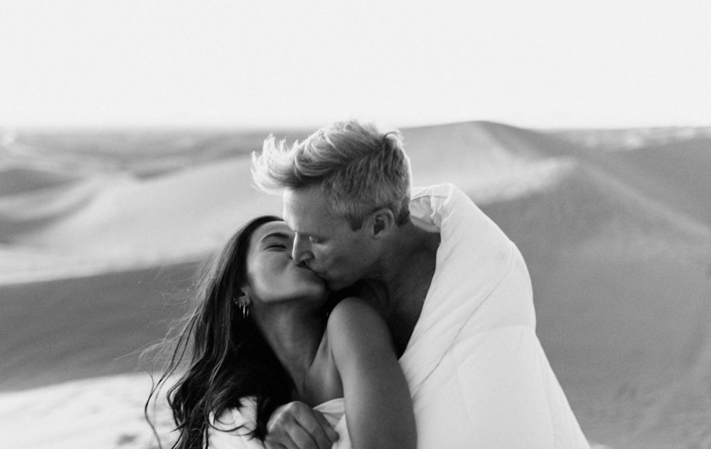 grayscale photo of man kissing woman on her cheek