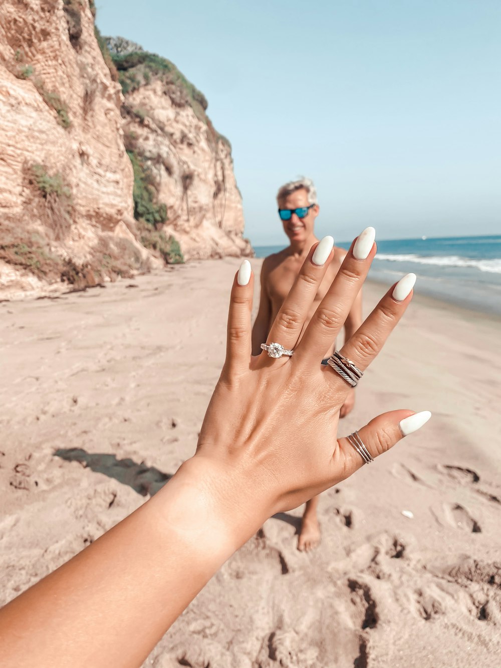 woman with blue manicure wearing silver ring on brown rock formation near sea during daytime