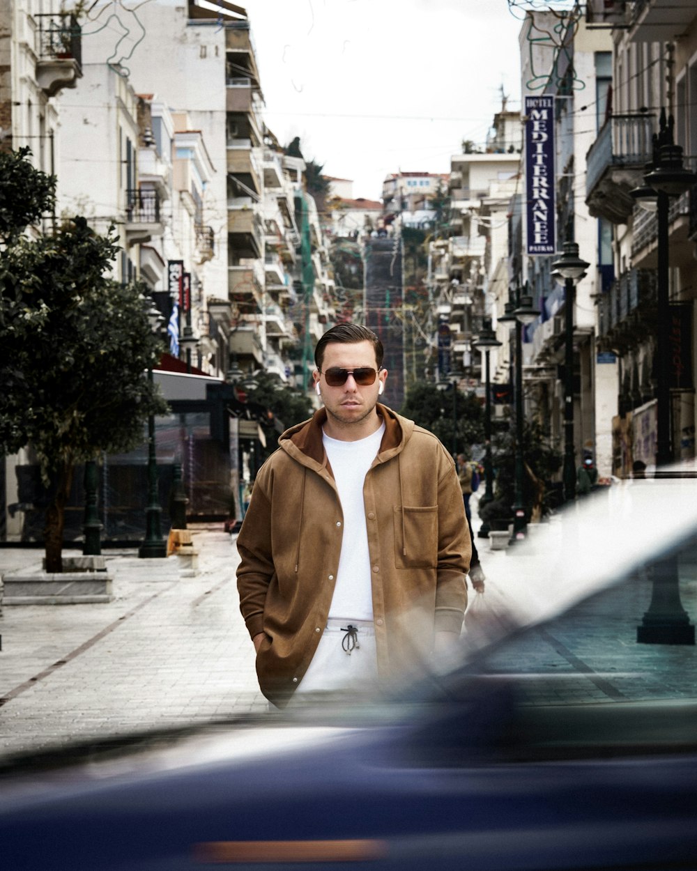 man in brown coat standing on sidewalk during daytime