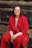 a woman in a red suit sitting on a tree stump