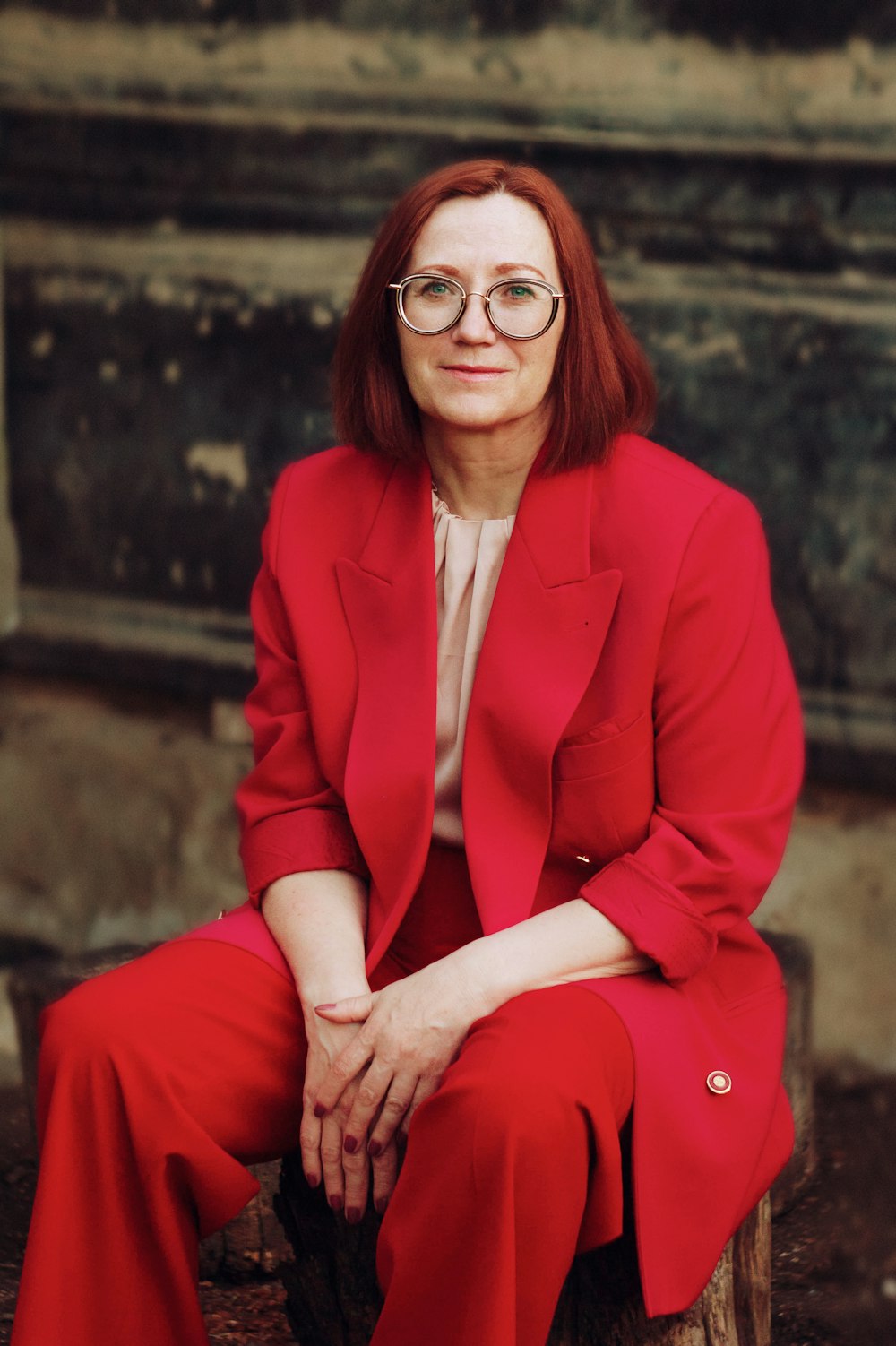 a woman in a red suit sitting on a tree stump