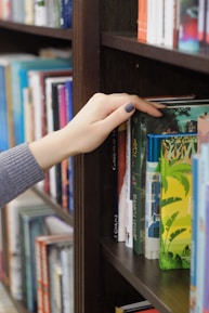 Close-up of a hand selecting a beautifully bound book from a shelf filled with artistic volumes.
