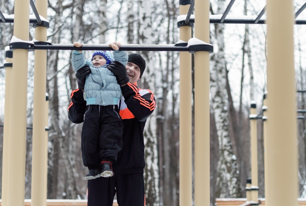 boy in red and black jacket standing on brown wooden swing during daytime