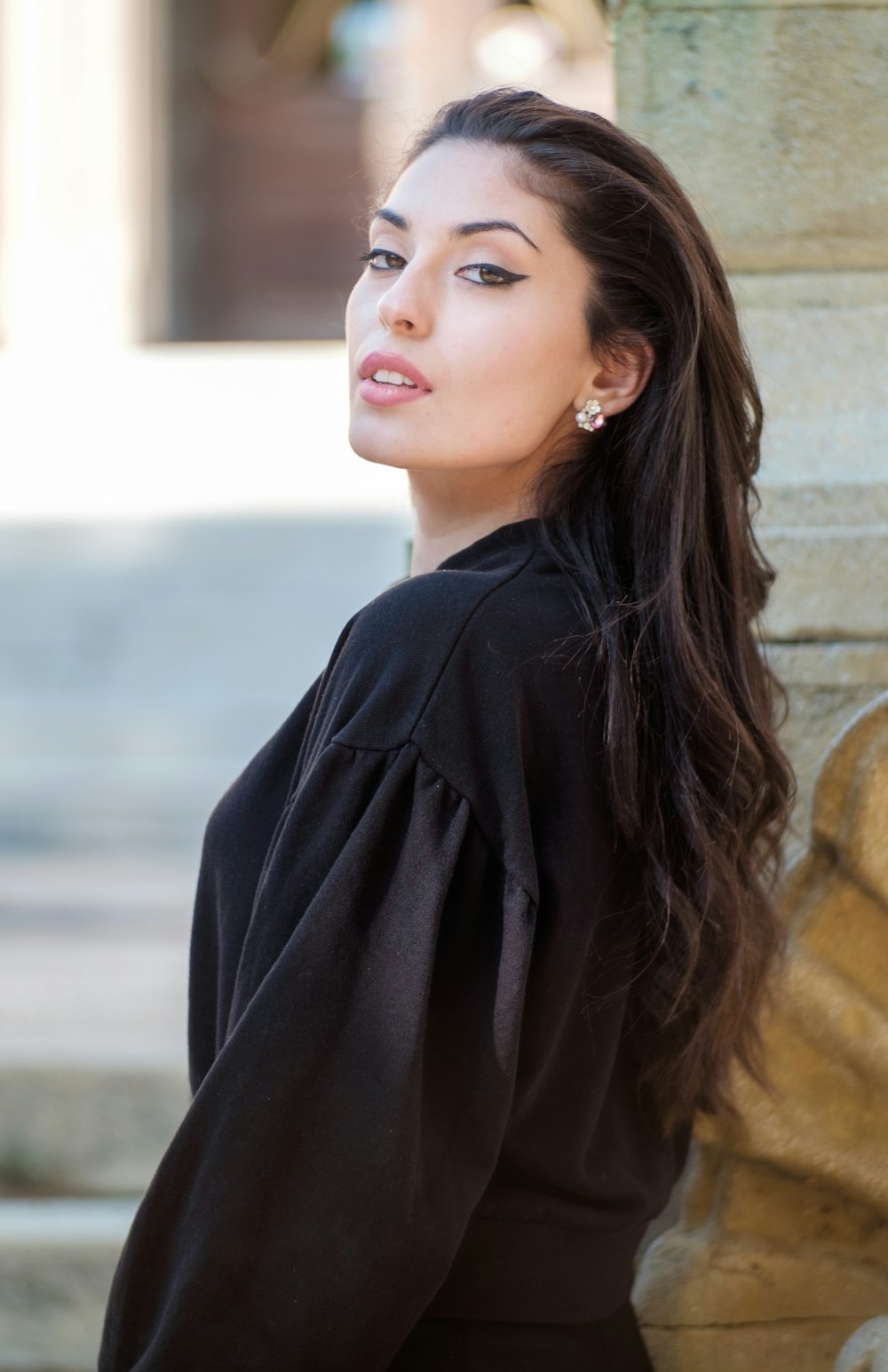 woman in black long sleeve shirt leaning on brown concrete wall during daytime