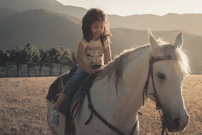 Crianca sorrindo em sessao de equoterapia em cima de cavalo branco ao ar livre