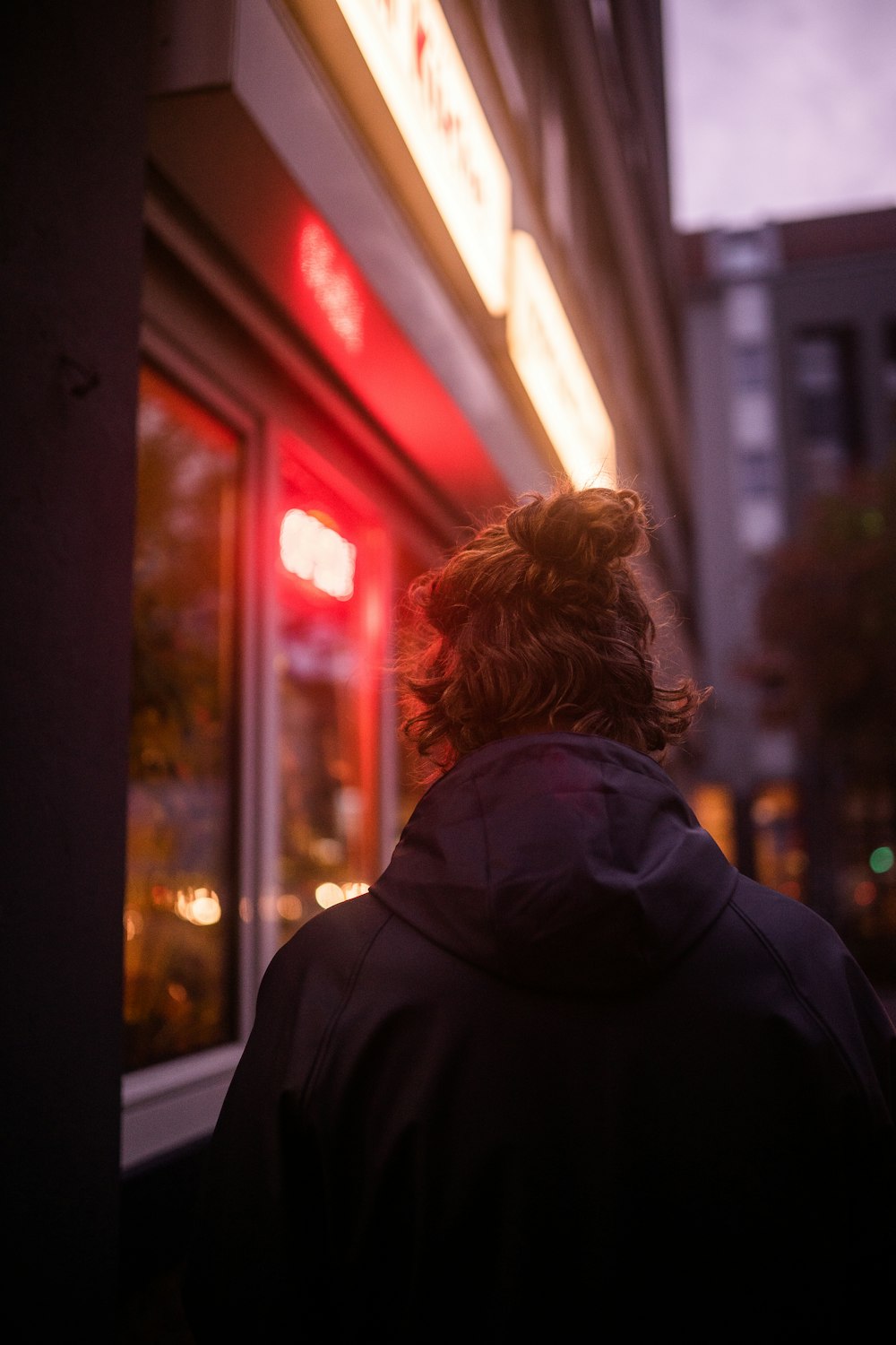 woman in black hoodie standing near glass window during night time