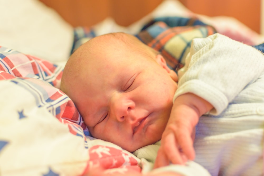 baby in white and blue onesie lying on bed