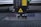 A laser engraving or cutting machine is positioned above a metallic surface, with its nozzle directed downward. The machine features warning labels, and the environment appears industrial, with a grid-like surface underneath.