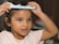 A child wearing a light-colored shirt is using a blue comb with cartoon designs to brush their hair. The child is focused and has a bracelet on one wrist, with a soft background out of focus.
