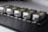 Five identical metallic devices are aligned in a row on a perforated black surface. Each device features warning labels and has a compact, industrial design, suggesting they are precision instruments or components used in an engineering or laboratory setting.
