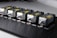 Five identical metallic devices are aligned in a row on a perforated black surface. Each device features warning labels and has a compact, industrial design, suggesting they are precision instruments or components used in an engineering or laboratory setting.