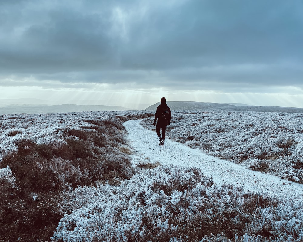 man in black jacket walking on snow covered field under cloudy sky during daytime