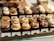 A display of various cupcakes neatly arranged on a wooden tray, each with different toppings and labels. The cupcakes include flavors like S'mores, Butterscotch Honeycomb, Salted Caramel, Milk Chocolate Banana, Chocolate Hazelnut, and Earl Grey. The toppings range from cookies and cream to nuts and swirls of frosting.