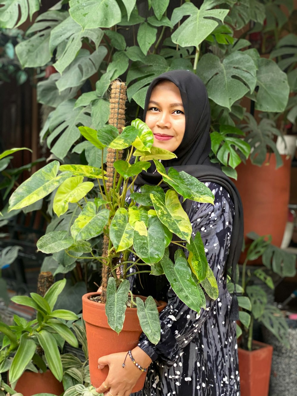 Frau im schwarzen Hijab steht tagsüber neben einer grünen Pflanze