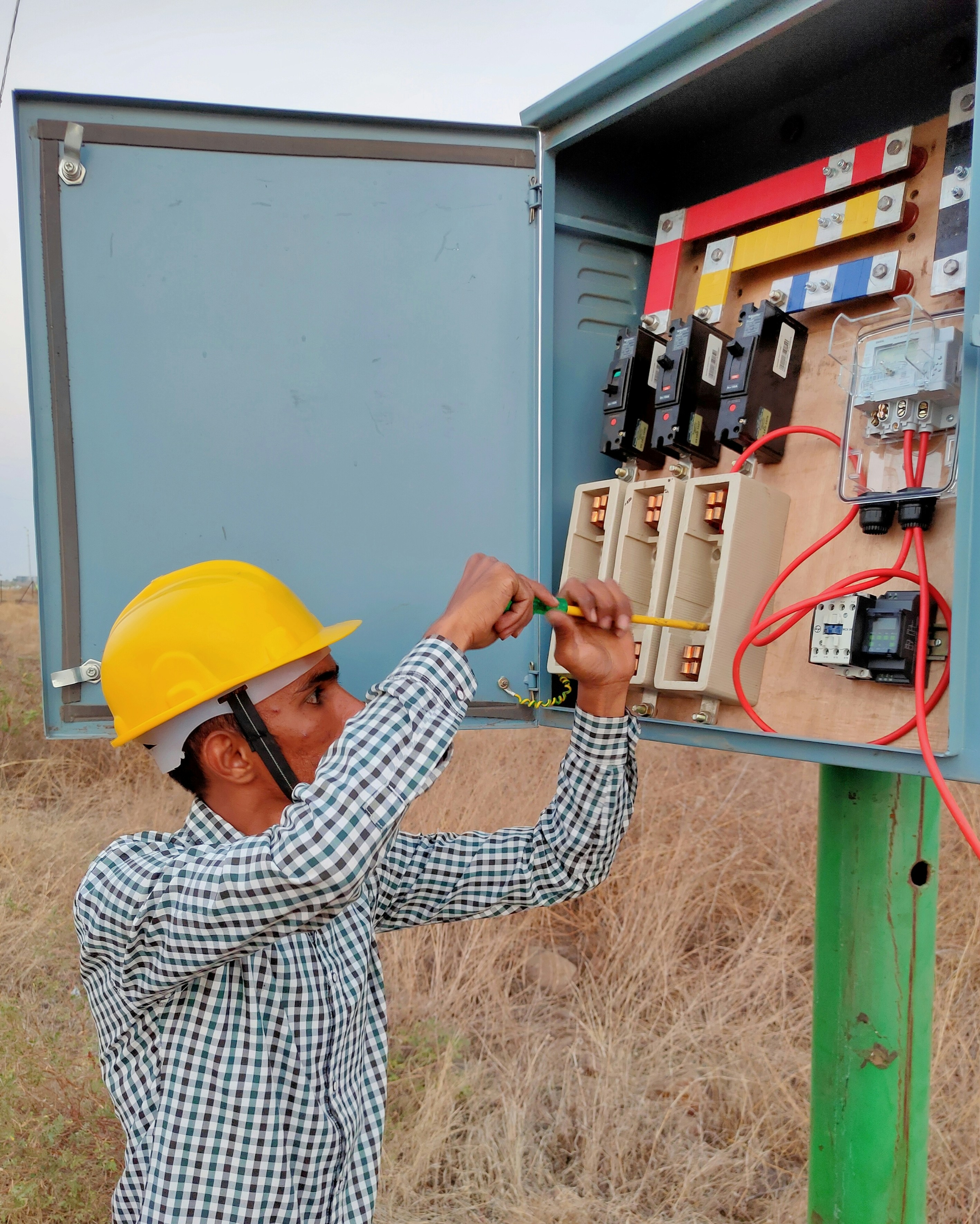 Professional electrician in hard hat working on commercial electrical panel outdoors in bright daylight