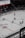A professional ice hockey match captured from a high vantage point, featuring players in red and white uniforms moving across the rink. The scene includes a large digital screen displaying a live feed of the game and a sparsely filled audience watching from the stands.