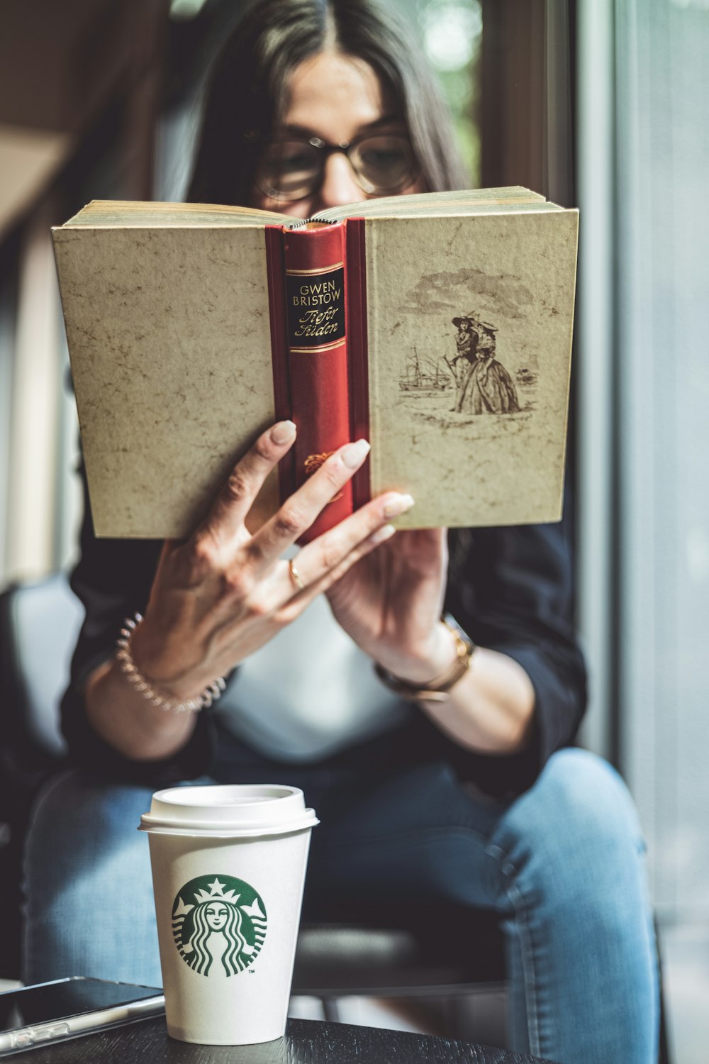 person holding brown book near white ceramic mug