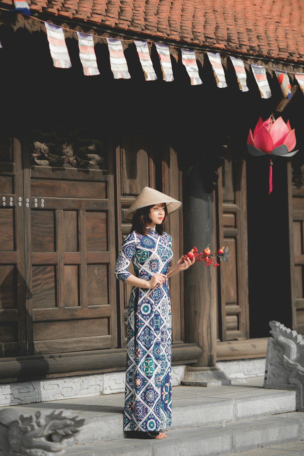 Mujer con vestido floral azul y blanco con sombrero negro de pie cerca de la puerta de madera marrón