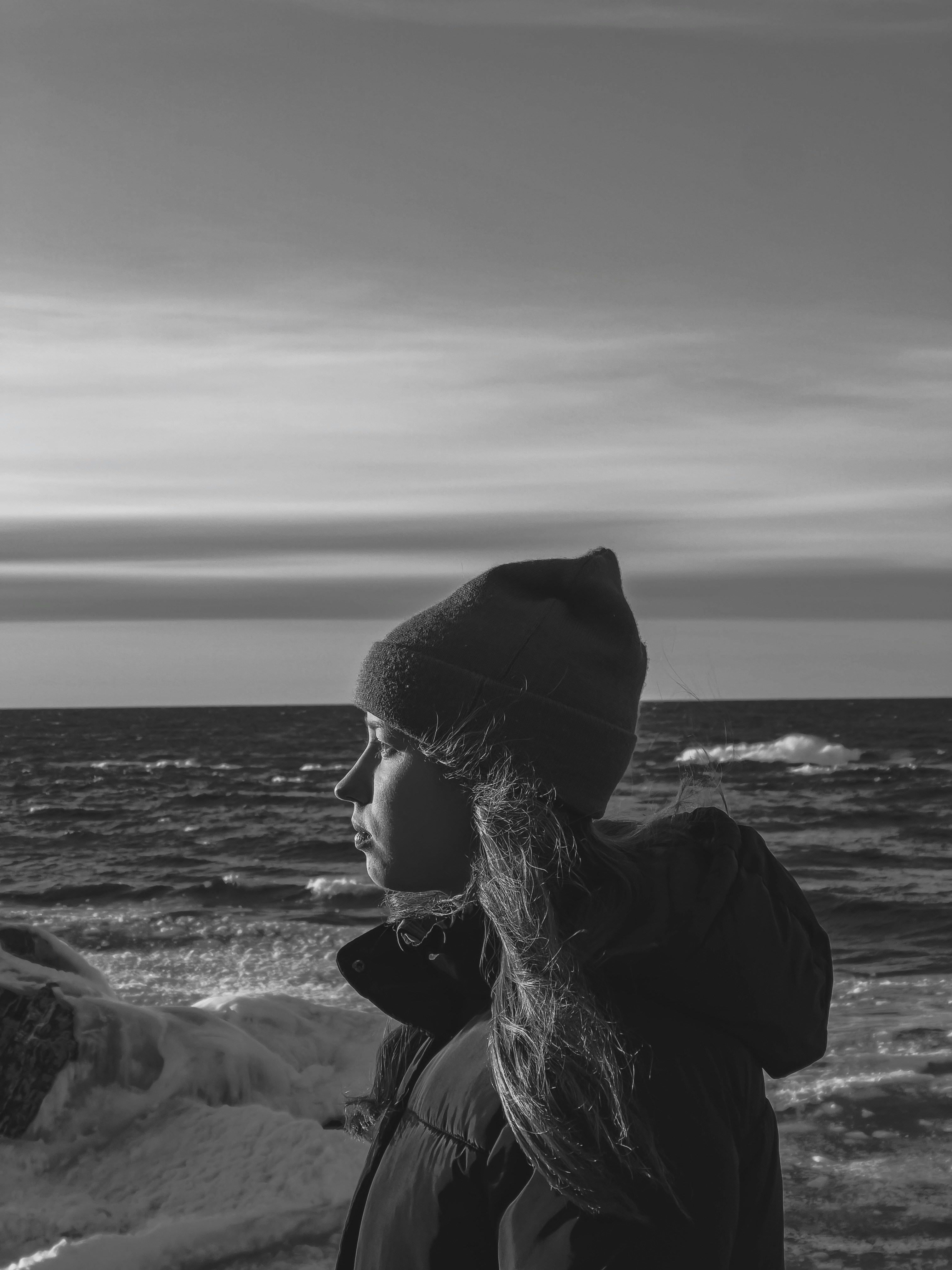 grayscale photo of woman in black hat and sunglasses near body of water