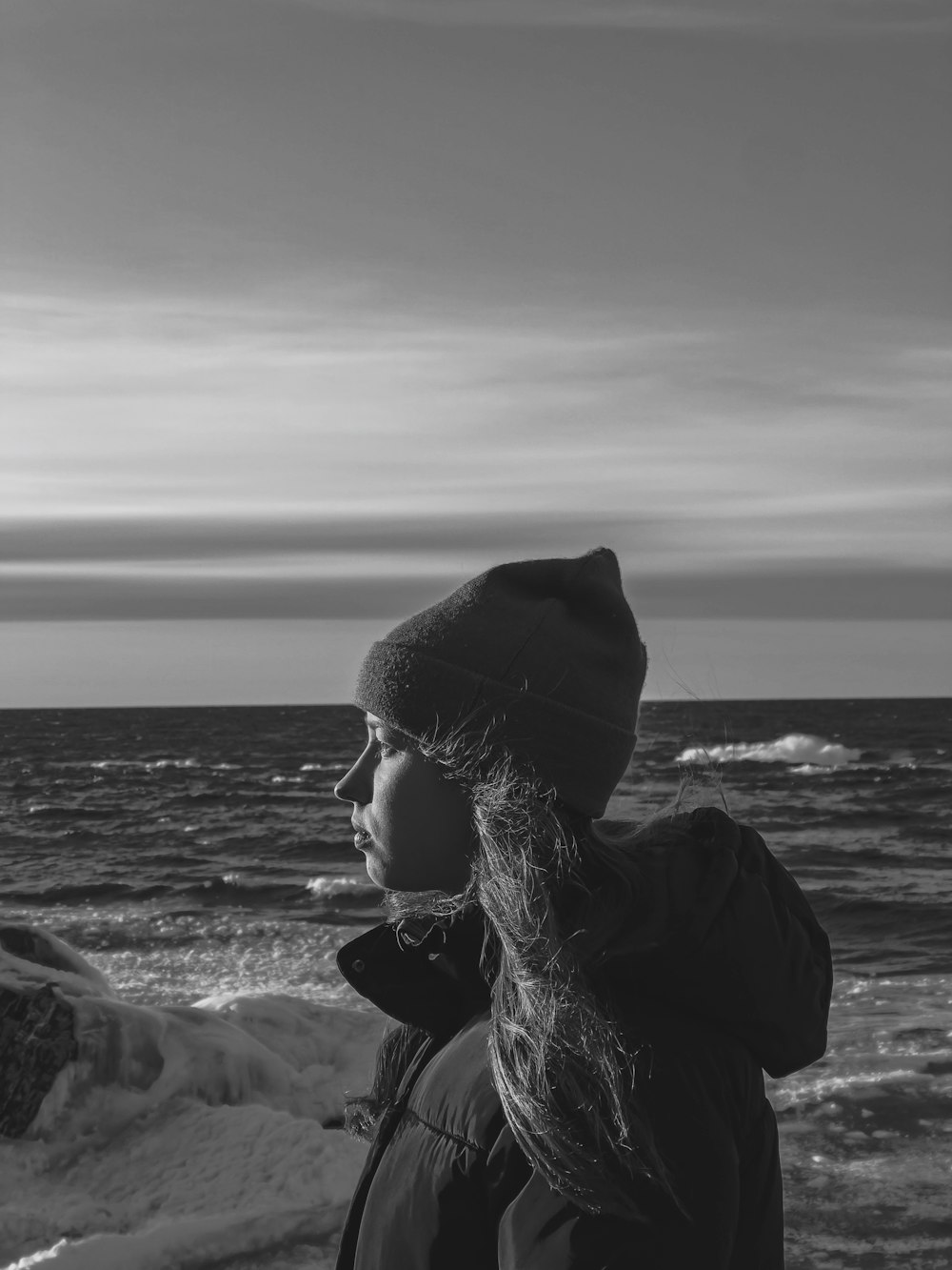 grayscale photo of woman in black hat and sunglasses near body of water