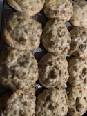 A tray of freshly baked biscuits topped with a mixture of sausage and cheese, slightly browned on top and filling the entire frame.