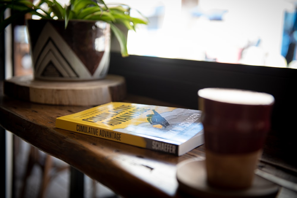 Libro azul y amarillo junto a taza de cerámica marrón sobre mesa de madera marrón