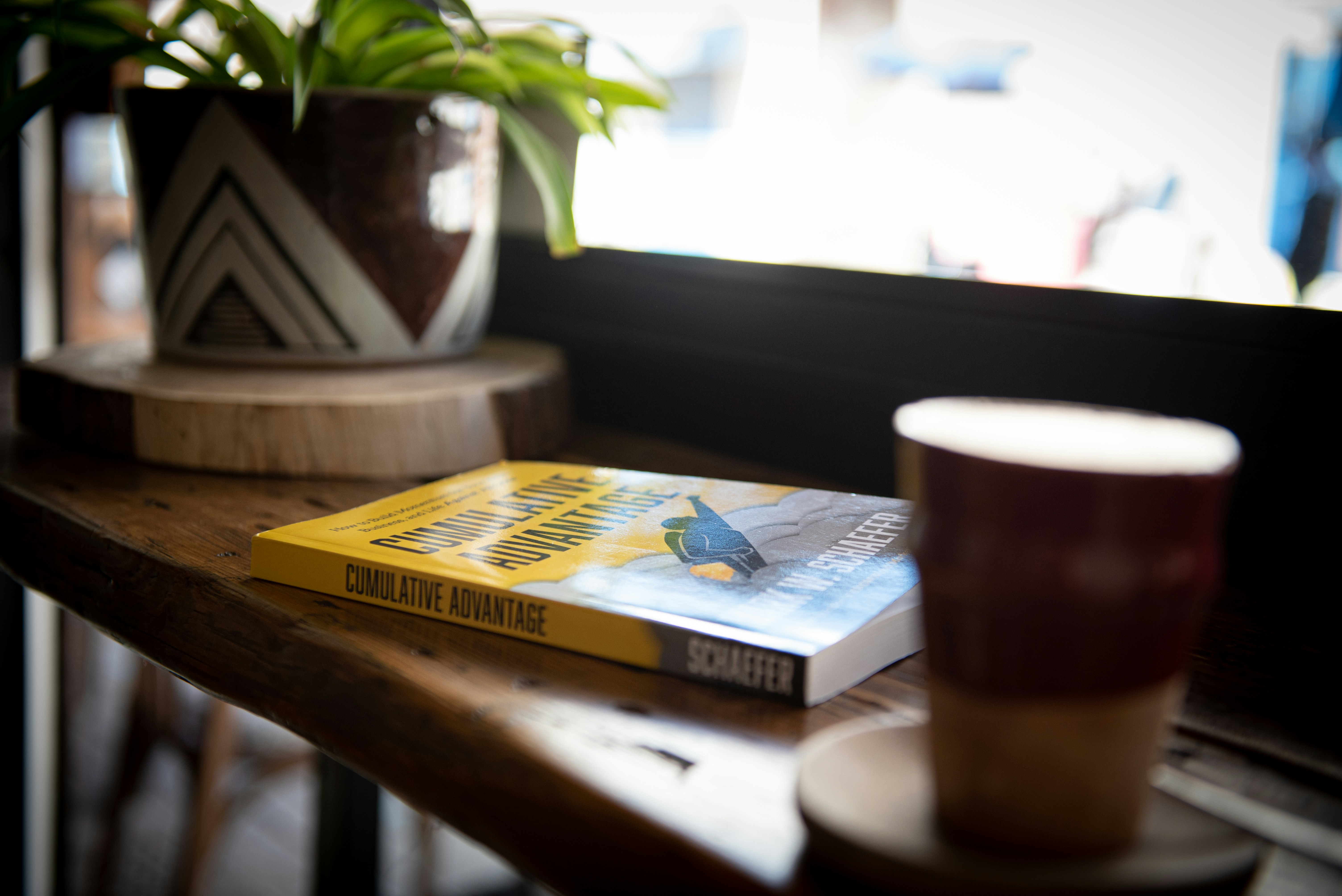 Rustic cafe scene: coffee, book, plant, blurry street background. Enjoy your reading!