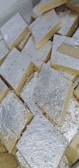 A collection of square-shaped sweets covered with a thin layer of silver foil, arranged closely together in a box.
