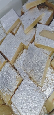 A collection of square-shaped sweets covered with a thin layer of silver foil, arranged closely together in a box.