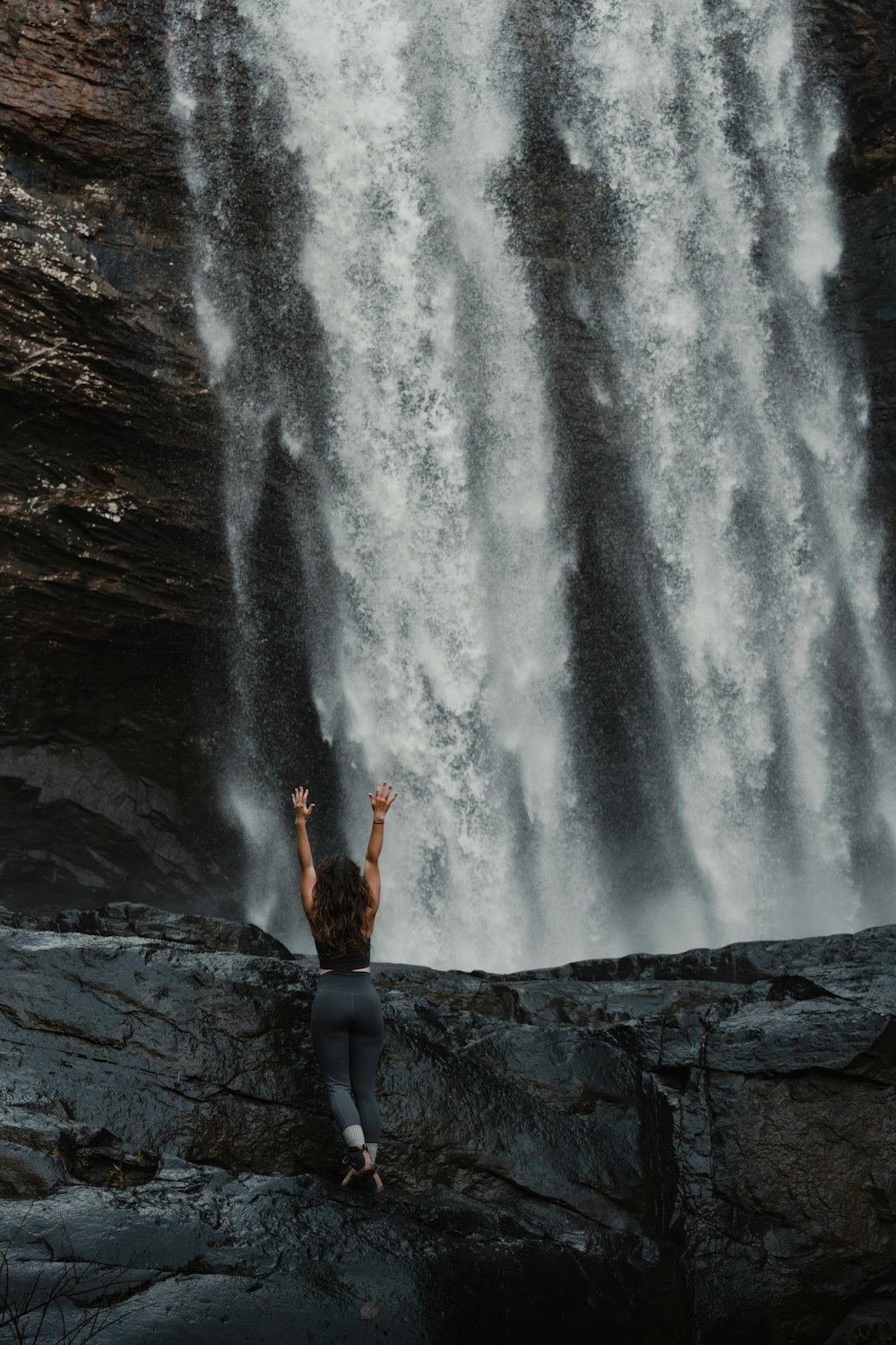 person in black pants standing on rock in front of waterfalls during daytime