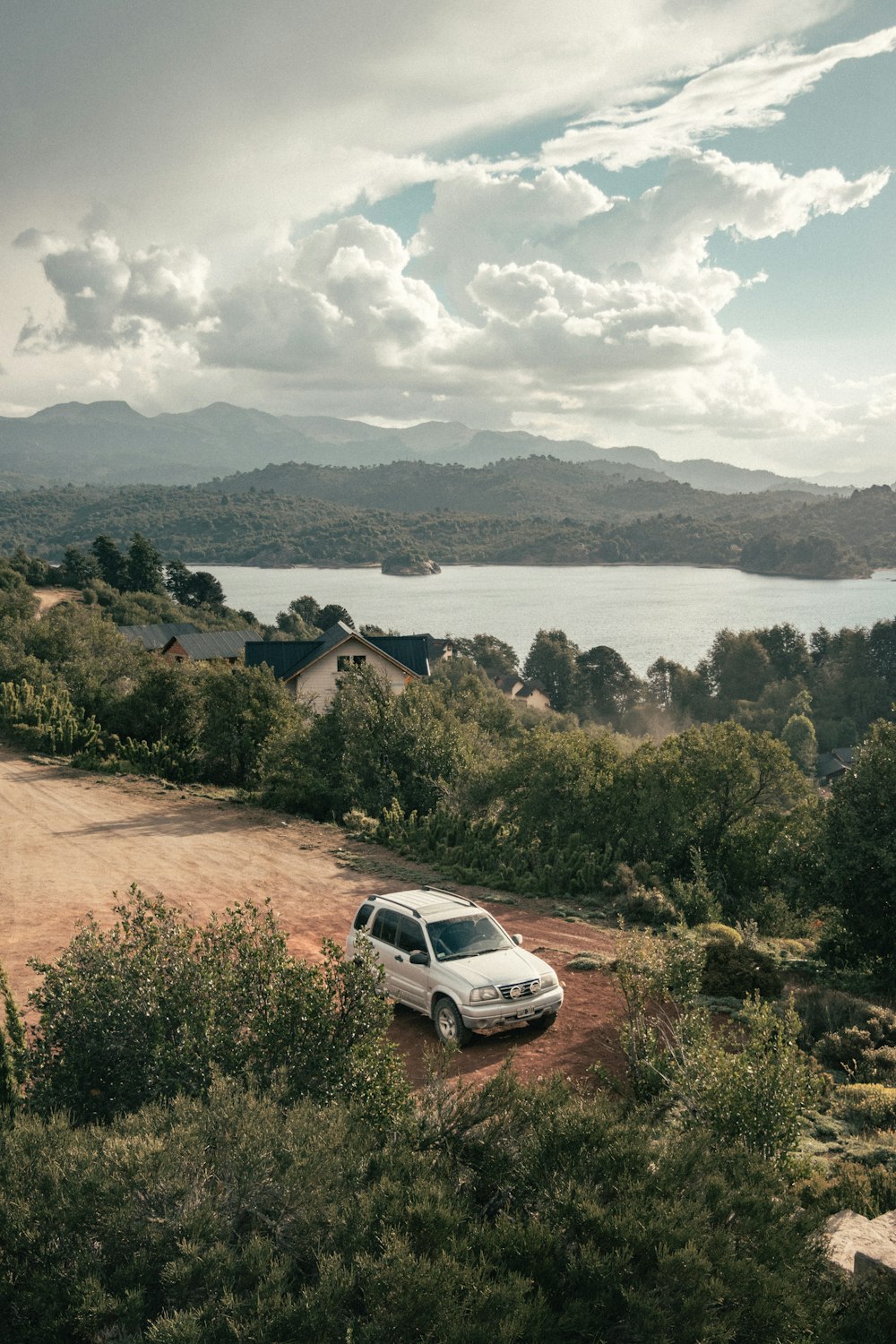 white car on road near green trees and body of water during daytime