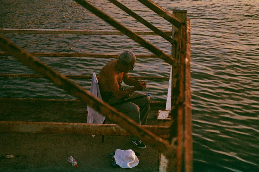 man in black shorts sitting on brown wooden dock during daytime