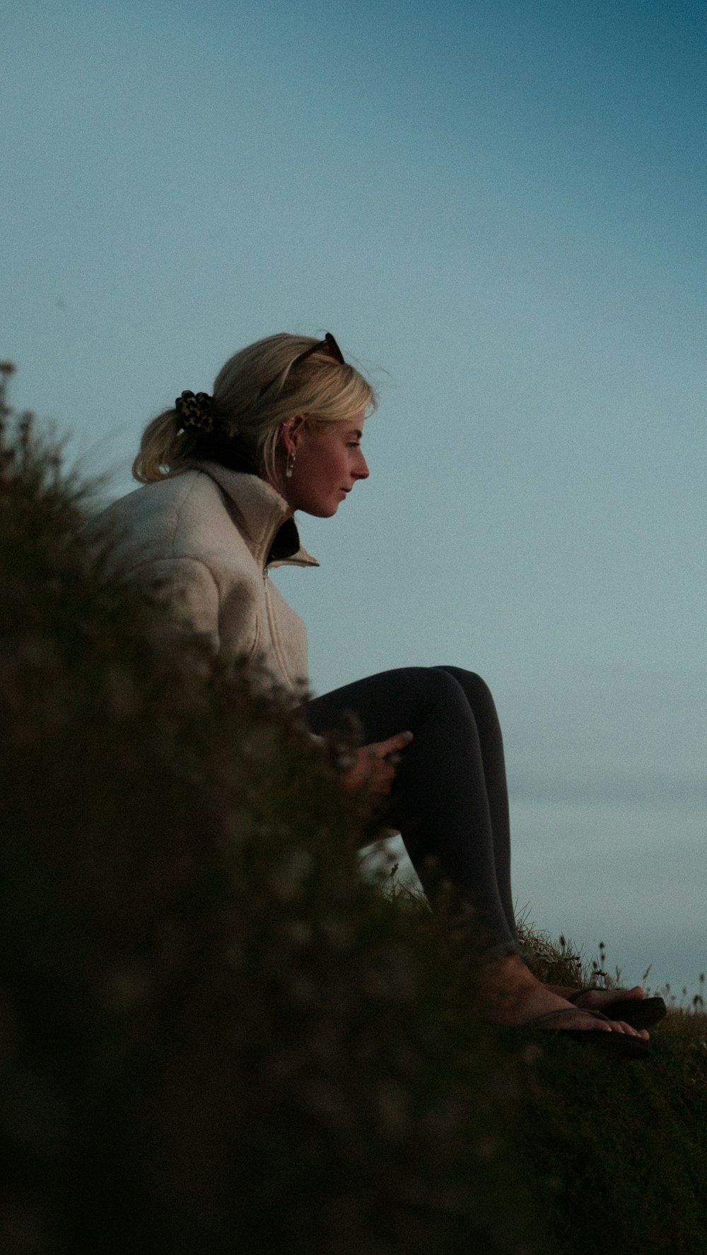 woman in brown coat and black pants sitting on green grass during daytime