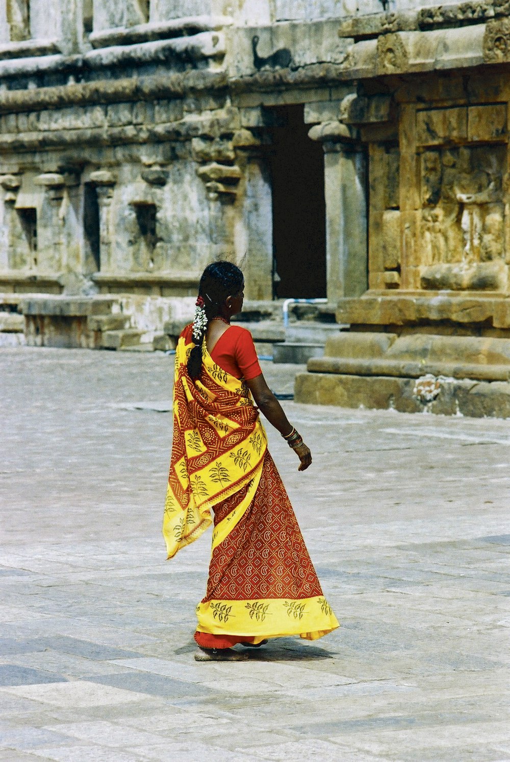 woman in yellow and red sari dress walking on white sand during daytime