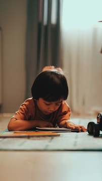 A young child focused on reading a colorful book in a bright classroom.