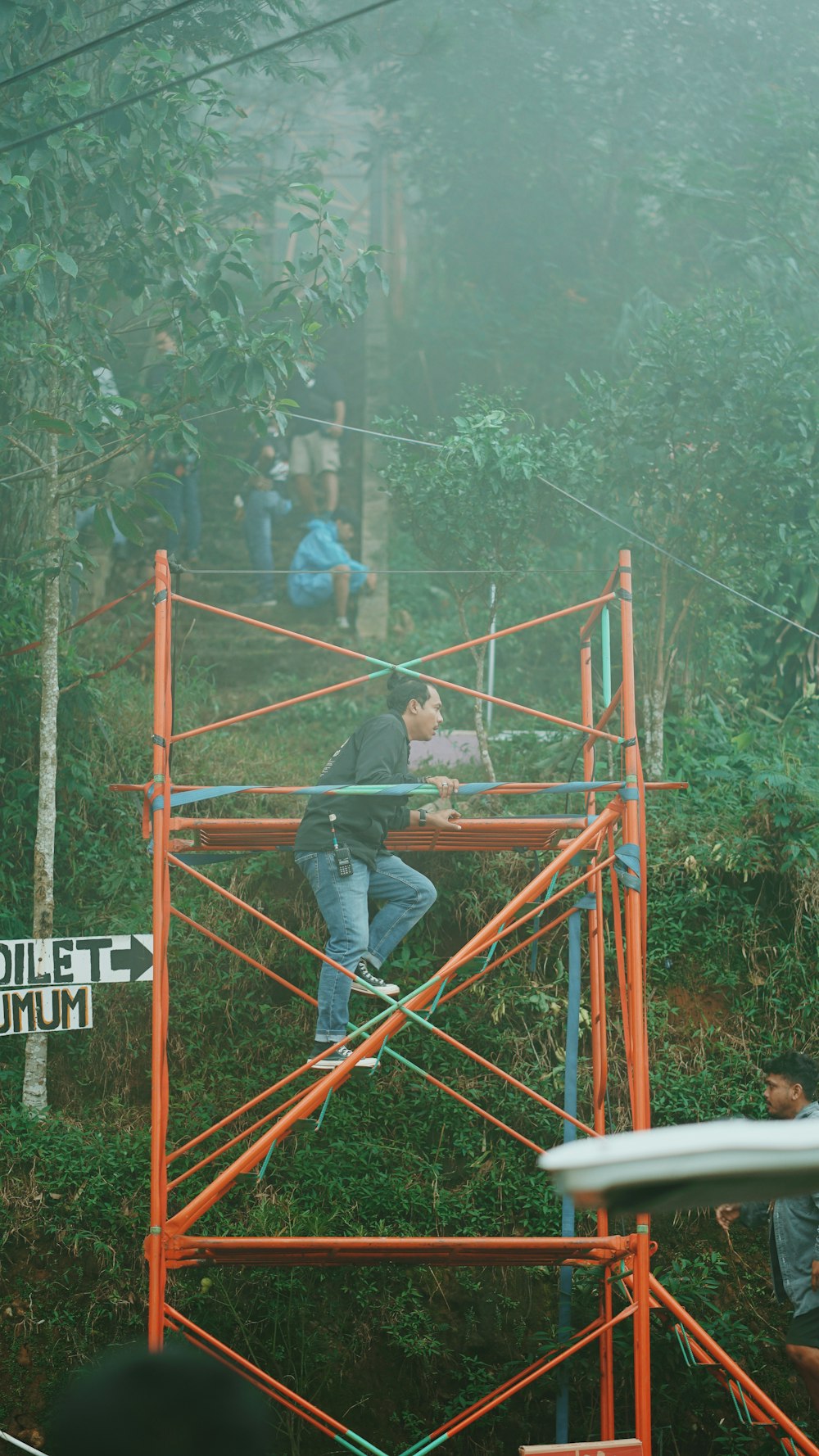 man in blue jacket sitting on red metal ladder