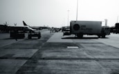 An airport tarmac with several parked aircraft from SpiceJet and a catering truck labeled 'LSG Sky Chefs'. The scene is busy with airport personnel and various ground service equipment visible. The image appears to be taken on a clear day with a control tower in the background.